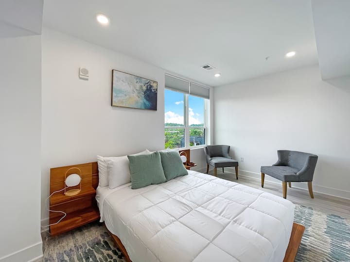 Chambre avec literie blanche, oreillers d'appoint, chaises et design moderne et lumineux.