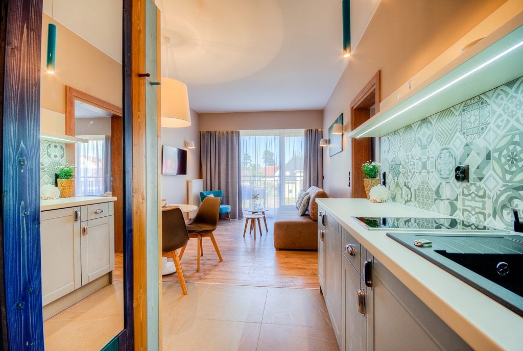 A modern kitchenette is visible, equipped with sleek cabinetry and counter space. The open living area features a comfortable sofa, a round coffee table, and dining chairs. Large windows allow natural light to fill the space, creating a warm ambiance.