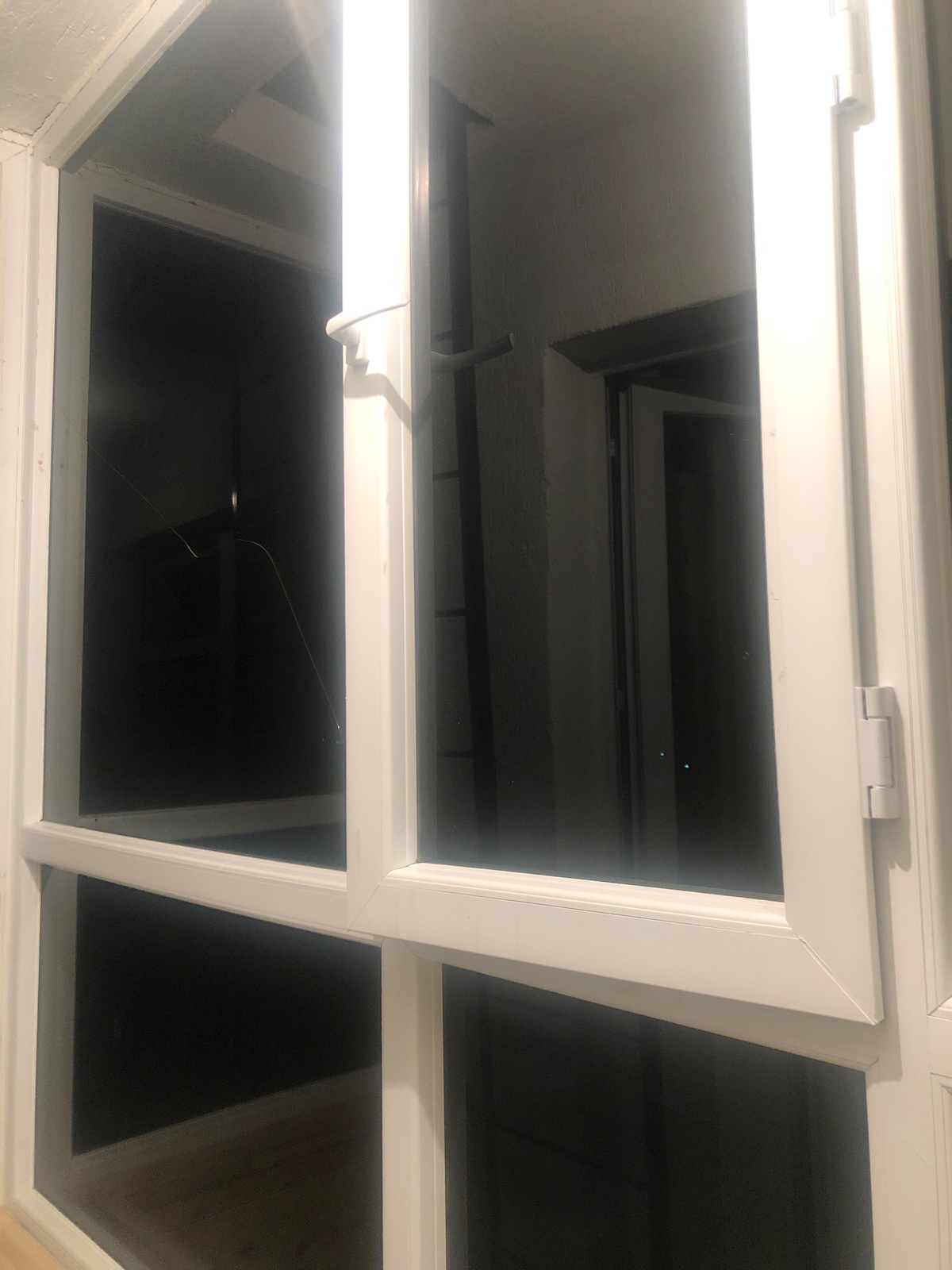 A white-framed window is shown, partially open to reveal a view into a darkened space. The sleek design emphasizes the minimalist aesthetic of the surroundings, allowing for natural light while maintaining privacy.