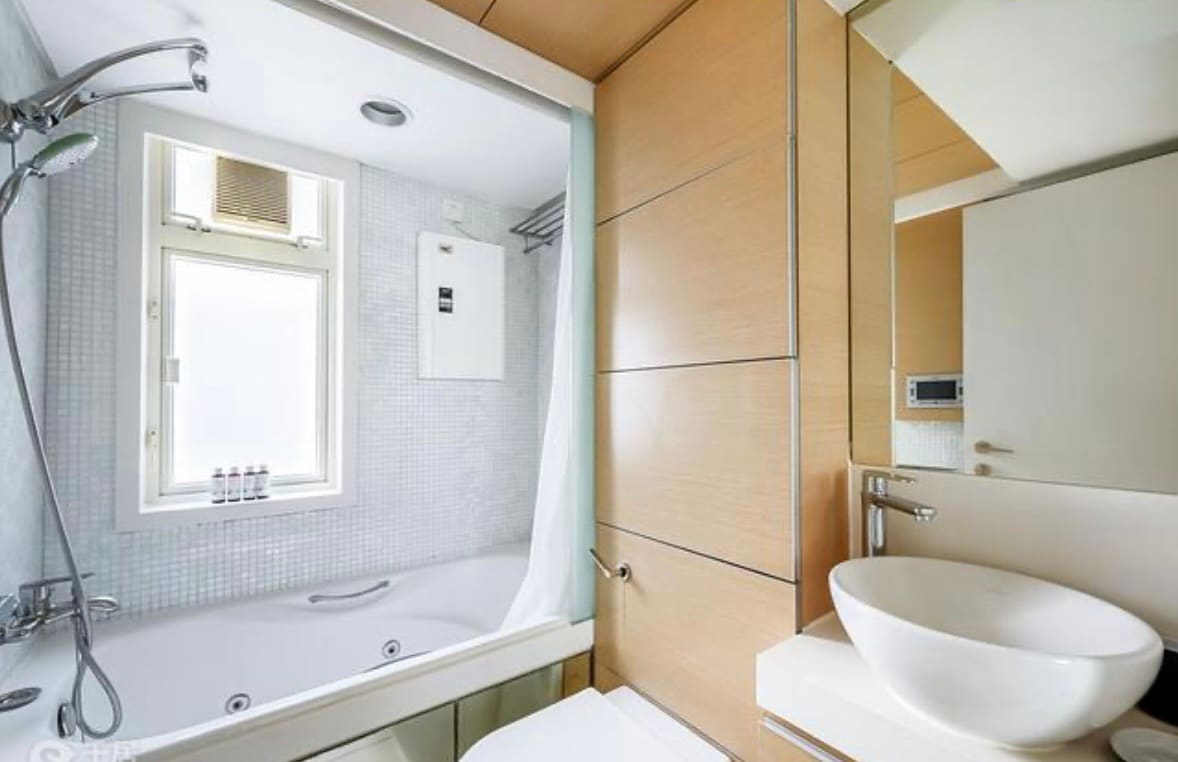 A modern bathroom features a spacious bathtub with a showerhead overhead. Light enters through a window above the tub, while a sleek vessel sink is positioned on a minimalist countertop. Neutral tones and streamlined cabinetry contribute to the contemporary design.
