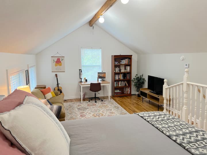 Уютно таванско помещение на горния етаж с работно пространство, диван, телевизор и легло.