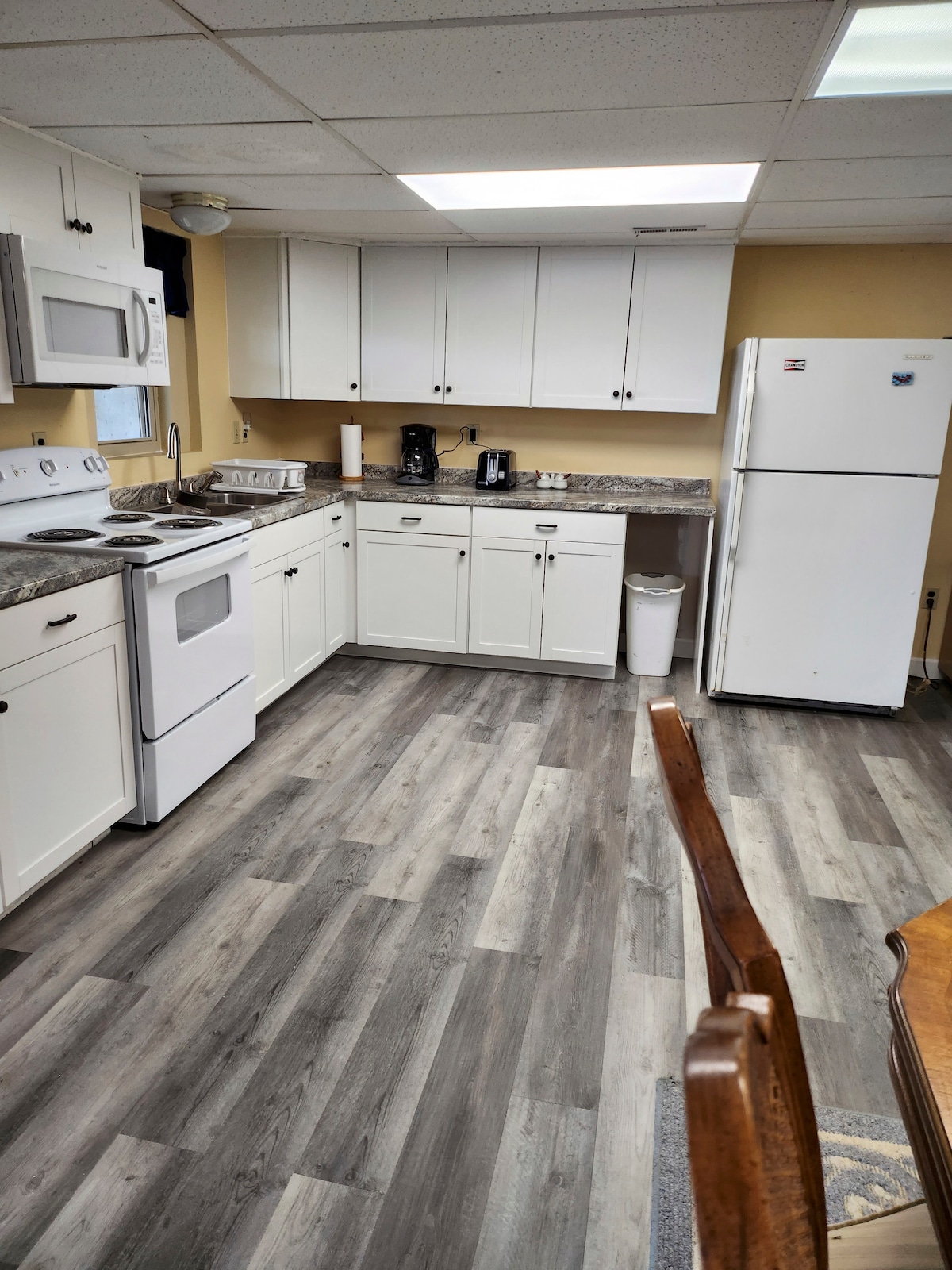 The kitchen area features white cabinetry paired with a granite countertop. A refrigerator, microwave, and oven are included among the appliances. Ample storage is provided with overhead cabinets, and the space is illuminated by fluorescent ceiling lights.