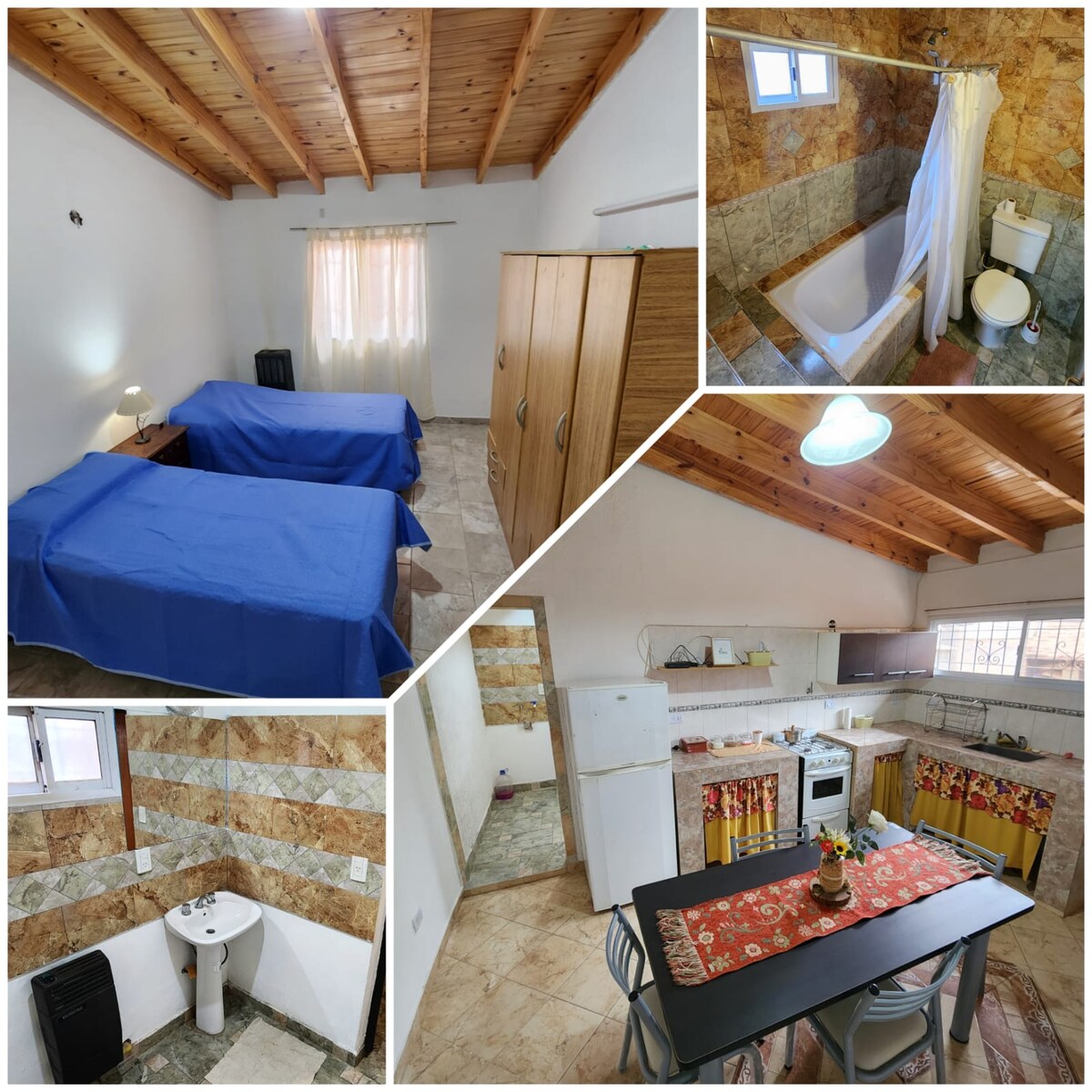 The image showcases a spacious room with two neatly arranged beds, each covered in blue bedding. A large window allows natural light to illuminate the room. A wooden wardrobe stands against a wall, and a bathroom area is partially visible with a bathtub and toilet.