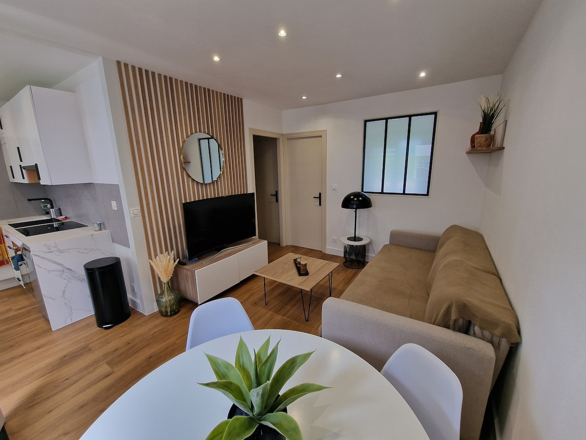 A modern living area is presented with a beige sofa and a wooden coffee table, complemented by clean lines and minimalistic decor. Light wood flooring runs throughout, while a round dining table with white chairs is visible beside a kitchen area featuring stylish cabinetry.