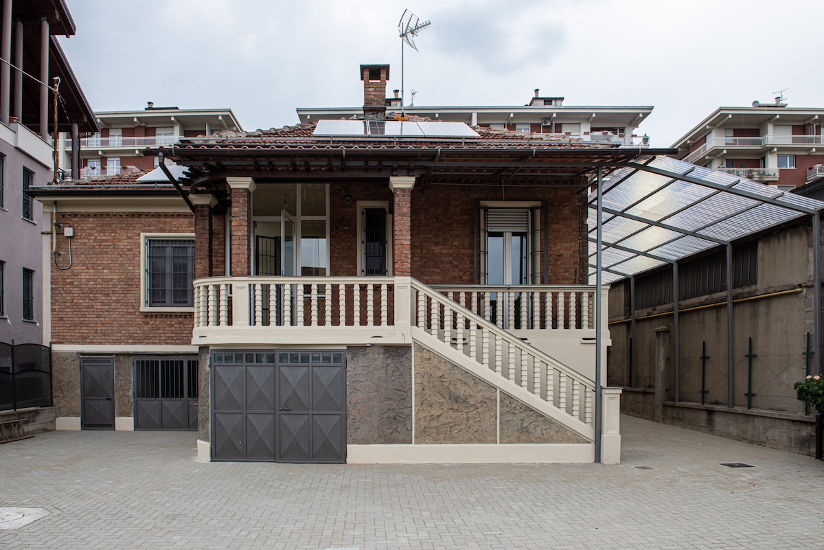 A newly renovated, independent building is depicted, showcasing a brick facade with white accents. A covered patio area can be seen, along with stairs leading to the entrance. The surrounding space is paved, providing a driveway and easy access to the property.