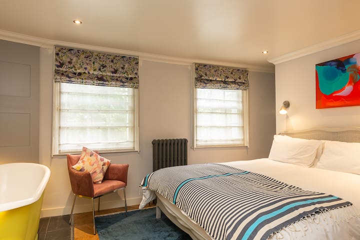 Dormitorio principal con una cama extra cómoda de tamaño superrejo y una profunda bañera de hierro fundido independiente. Hermosas vistas de la plaza del jardín