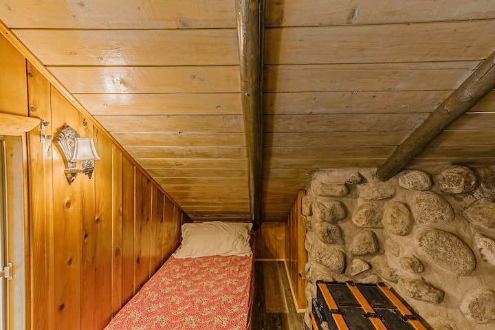 Удобен единечен кревет сместен под низок дрвен таван со рустикални камени ѕидни акценти.