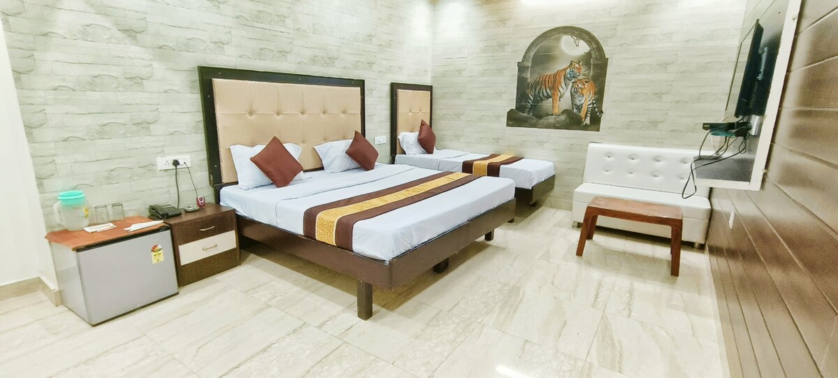 The room features two spacious beds with decorative headboards, complemented by brown accent pillows. A smooth, light-colored wall showcases an artistic tiger mural, while a sleek TV is mounted on the wood-paneled side. A white sofa and a small table are included for additional seating.