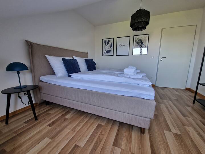 Dormitorio con cama de somier de 180x200 y hermosas almohadas decorativas azules, fotos azules y lámpara azul junto a la cama.