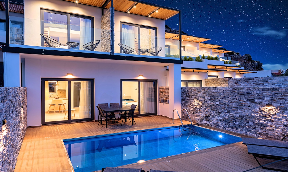A modern exterior showcases a private pool bordered by a wooden deck. Multiple seating areas are arranged, offering views towards the house's glass doors. The upper floor includes balconies with stylish seating, while stone accents add texture to the contemporary design.