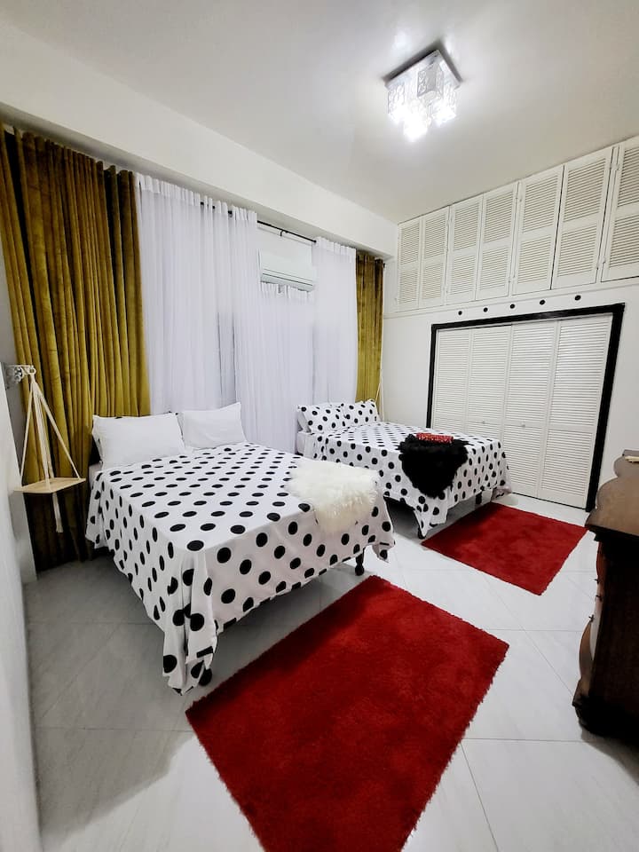 This bedroom sleeps 4 guests and is adorned with luxurious golden curtains and soft white drapes, creating a warm and inviting atmosphere. The vibrant red rugs add a pop of color, enhancing the room's charm. 
