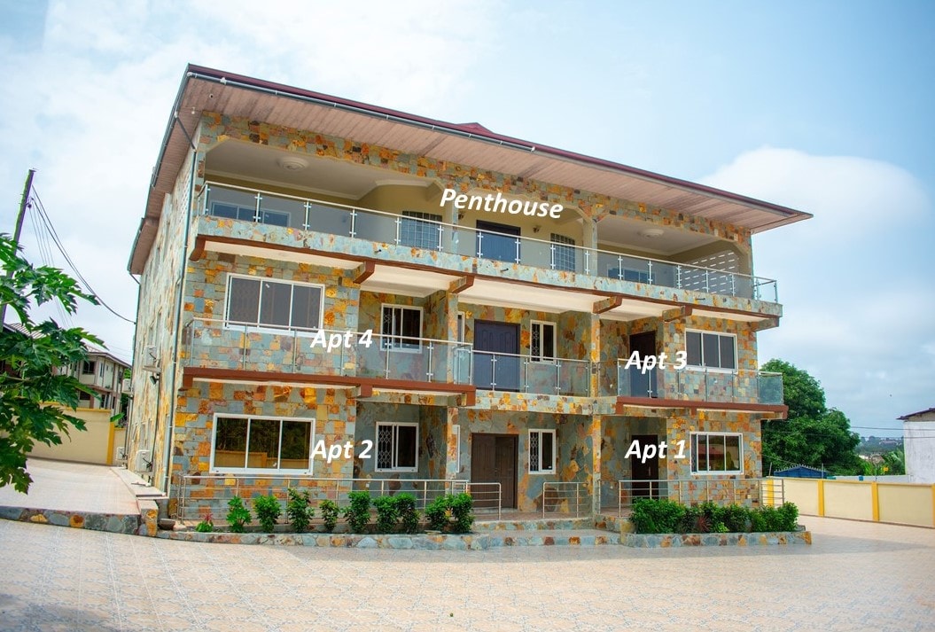A three-story building with a modern stone facade is featured, showcasing five distinct apartments, including a penthouse at the top. Balconies with glass railings are visible, along with a paved courtyard and surrounding greenery, providing a welcoming exterior environment.