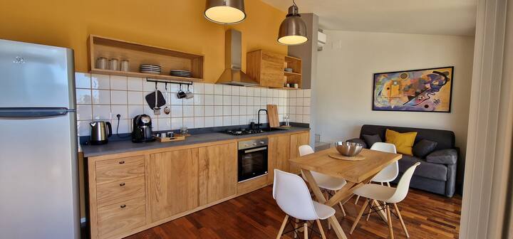 Cocina de diseño personalizado en madera de castaño con cocina, horno, hervidor eléctrico, cafetera. Mesa de comedor para 4 personas y sofá cama. 