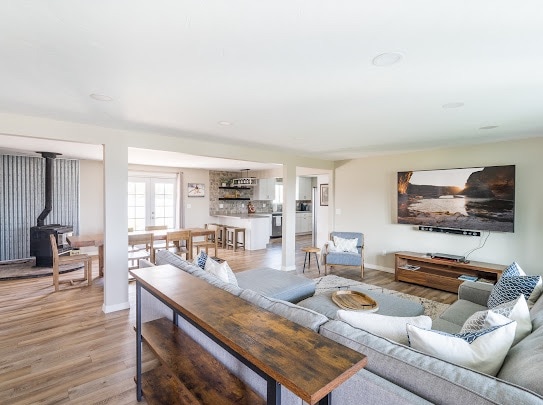 A spacious living area features a large sectional sofa adorned with decorative cushions. A wall-mounted television is positioned above a media console, while a dining table is visible in the background. Natural light floods through windows, enhancing the open layout.