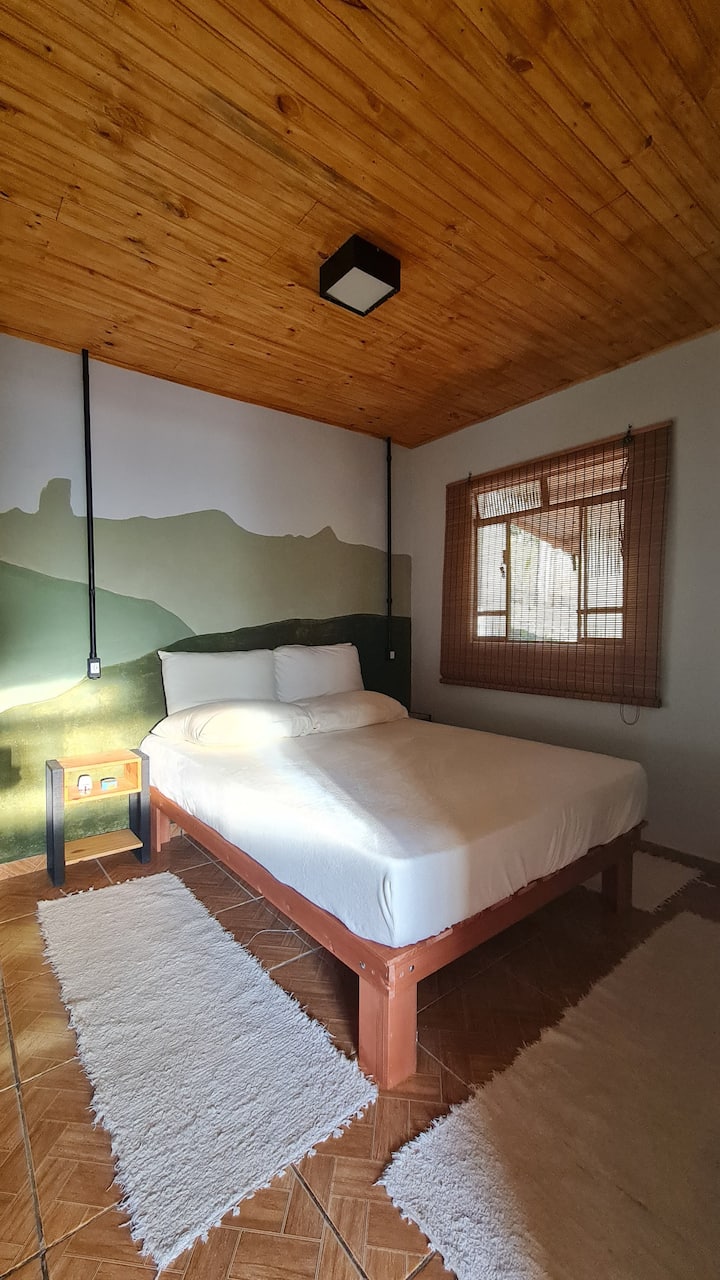 Quarto Pedra do Picu, com cama de casal, guarda-roupa, mesas de cabeceira,  espelho de corpo.