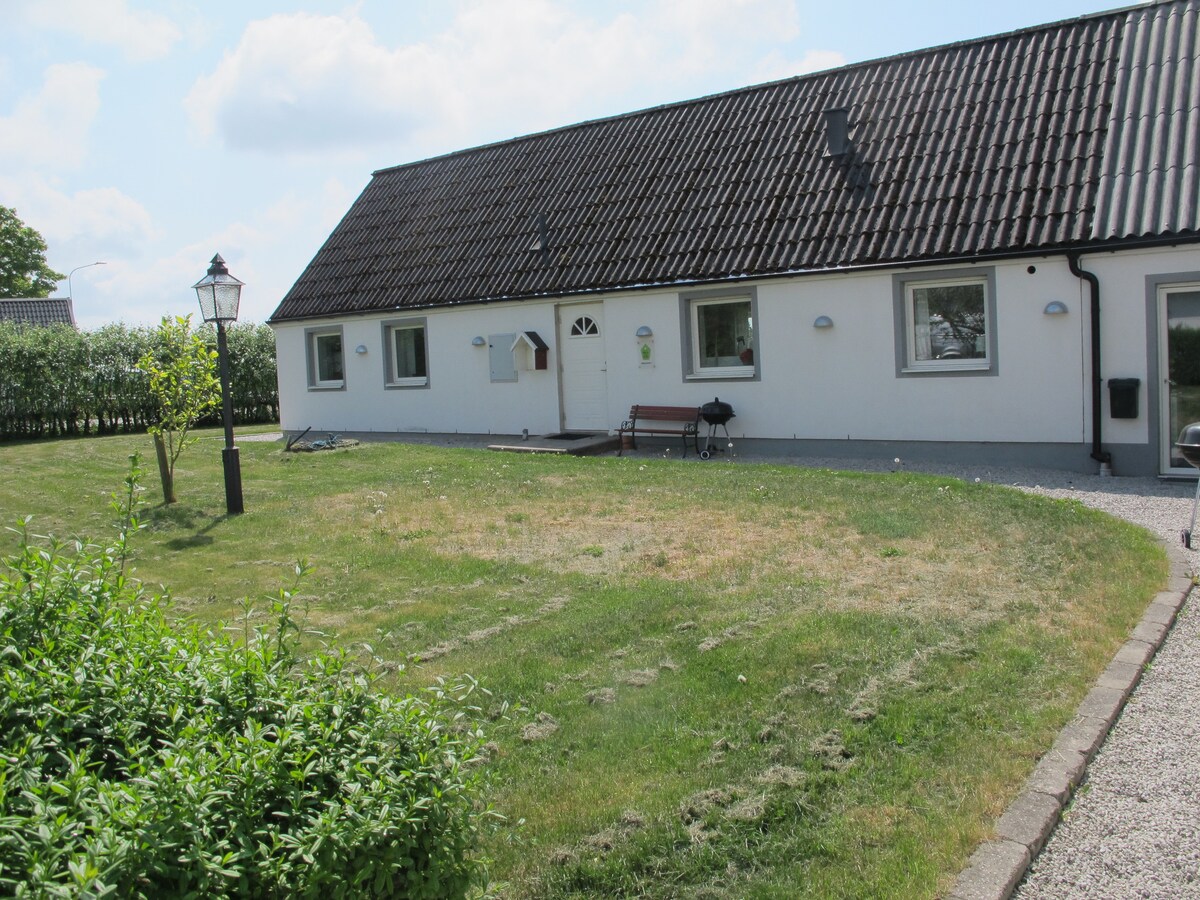 A well-maintained exterior shows a single-story building with a sloped roof. Green grass covers the front yard, while small shrubs and a bench add to the landscape. Outdoor lighting is provided by a traditional lamp post, enhancing the inviting atmosphere.