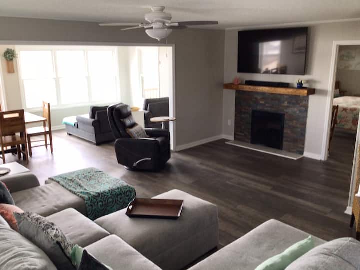 Gran habitación con televisor inteligente de 65pulgadas, chimenea de gas y vistas panorámicas al agua.