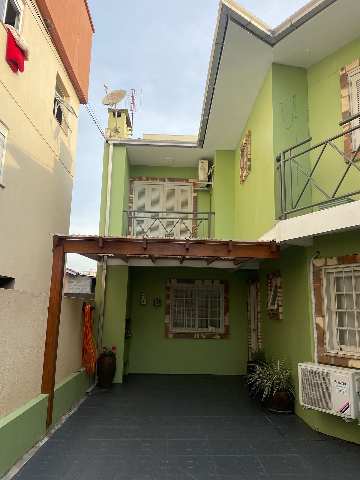 A green-painted building is partly visible, showcasing multiple levels and a covered outdoor area. The entrance area features a dark tiled floor, with plants and exterior air conditioning units adding to the modern appeal of the space.