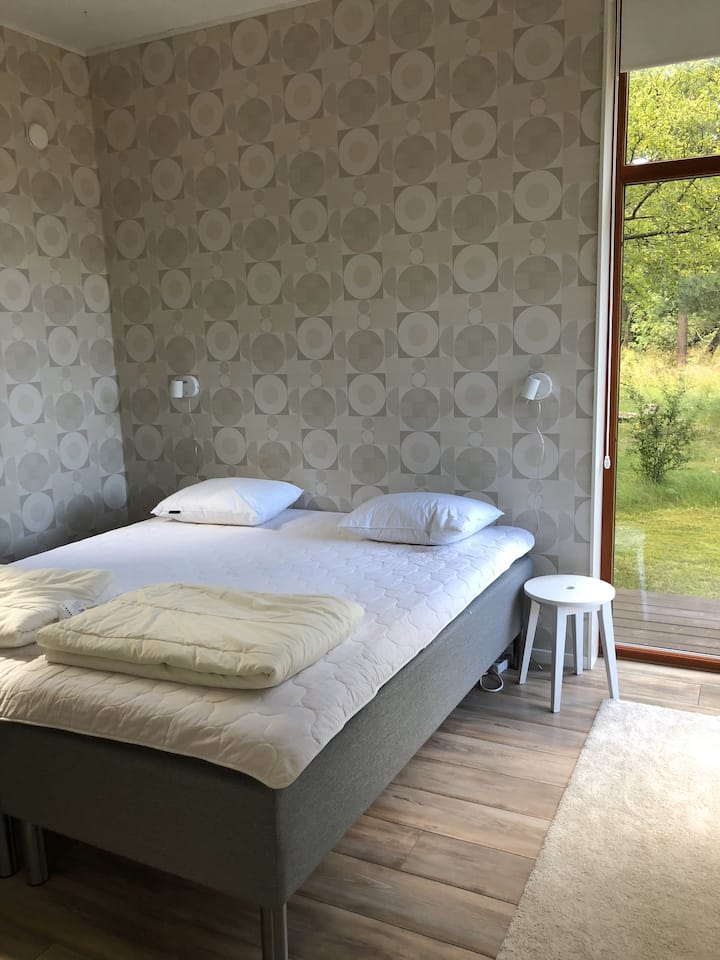 Dormitorio 4 con cama doble de 2 x 90 cm. Amplia ventana de esquina desde el piso al techo hasta la naturaleza.