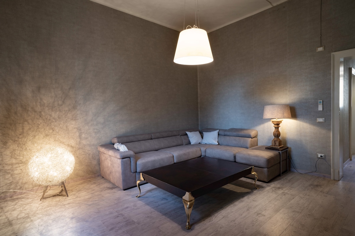 A spacious living area is highlighted by a contemporary L-shaped sofa and a large coffee table. A pendant light casts a warm glow, while a decorative lamp adds interest next to the sofa. Neutral tones create a calming ambiance in the room.