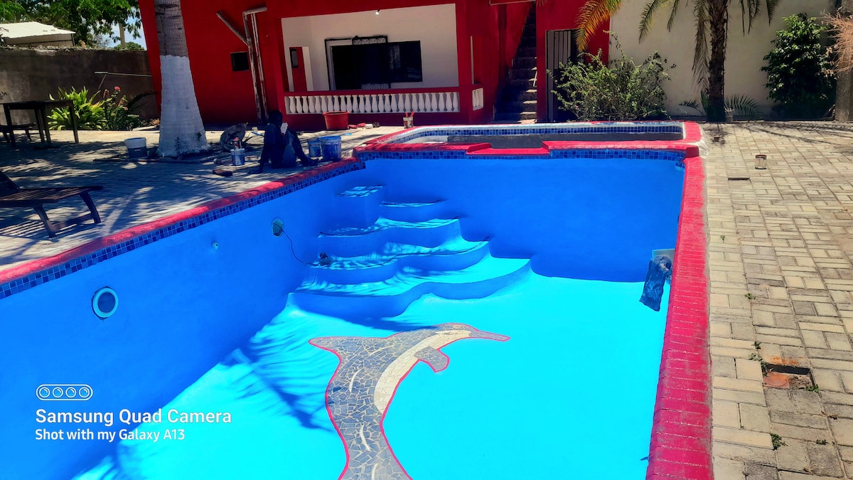 A pool area showcases an inviting swimming pool, featuring steps leading into the water. The pool's vibrant blue surface is complemented by colorful tile detailing along the perimeter. The surrounding patio area includes pavers and is bordered by tropical plants, enhancing the outdoor space.