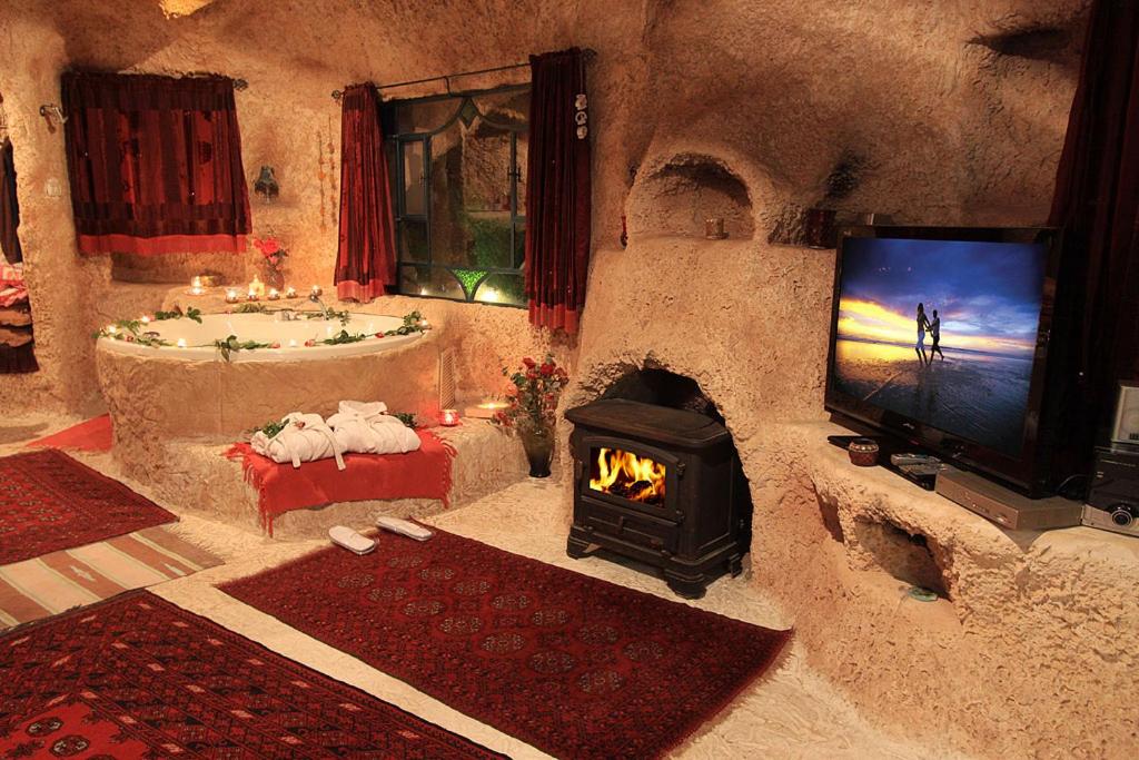A spacious cave unit features a cozy seating area with a fireplace and a television. A private jacuzzi is adorned with candles and flower arrangements. Decorative rugs cover the floor, and curtains frame the windows, providing a warm, inviting ambiance.