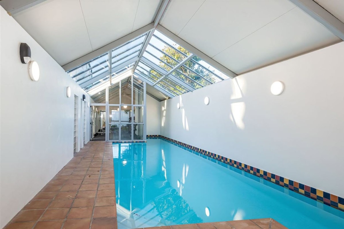 A well-lit indoor pool is featured, surrounded by large windows that allow natural light to stream in. The pool area is lined with colorful tiles, and the space is complemented by a clean, minimalist design.