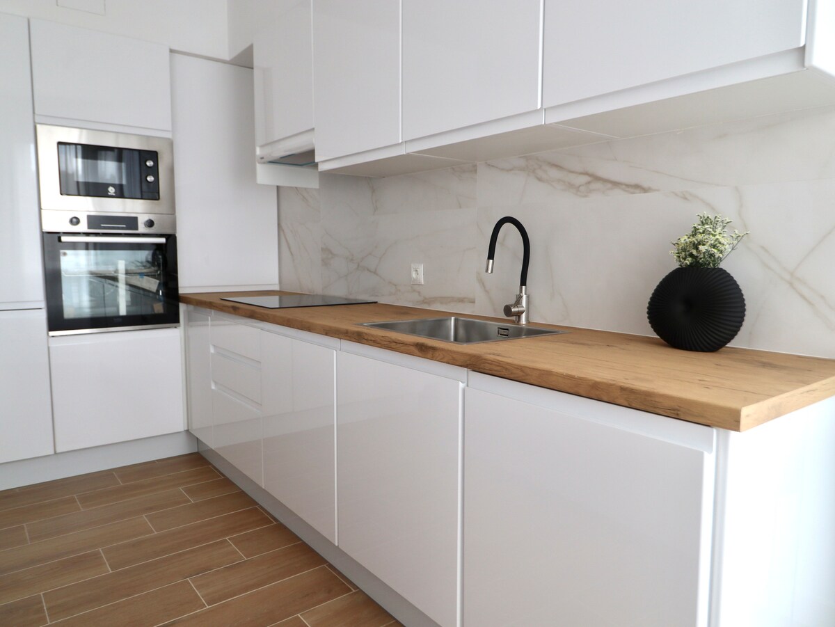 The kitchen features modern white cabinetry paired with a warm wooden countertop. Stainless steel appliances, including an oven and microwave, are positioned seamlessly within the design. A sleek sink is complemented by a contemporary black faucet, while a decorative vase adds a touch of elegance.