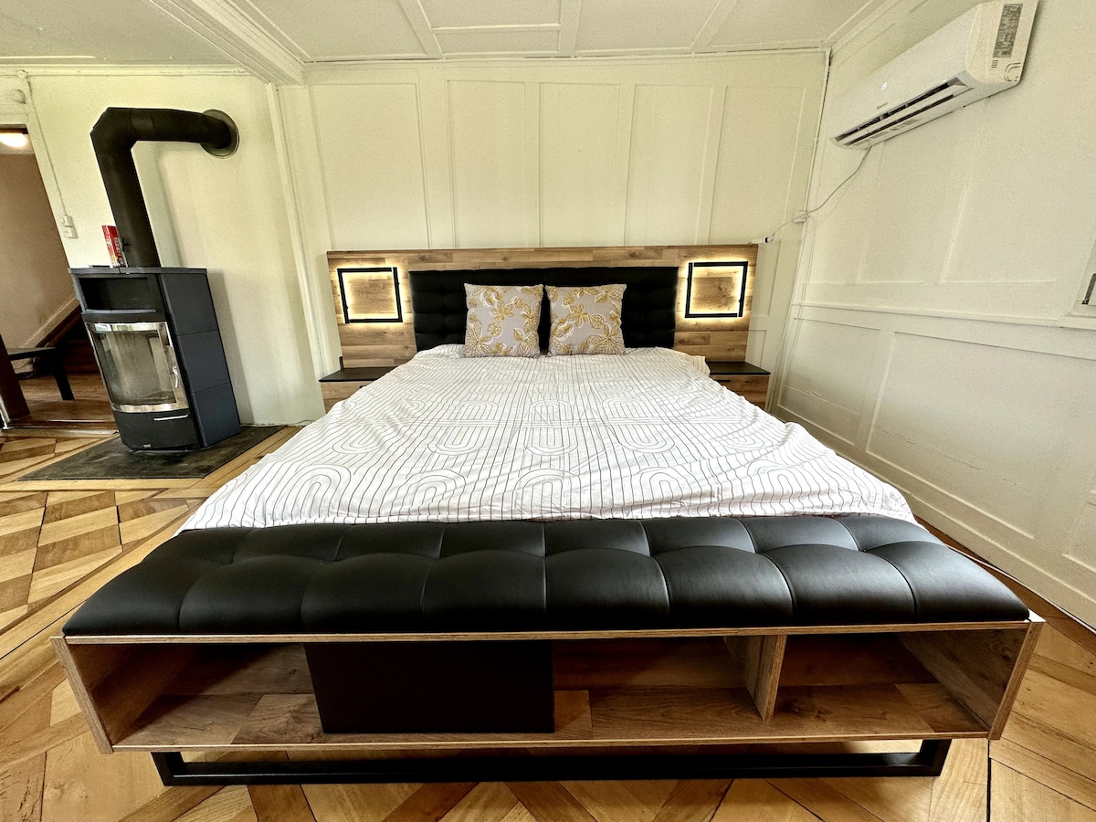 The spacious bed is framed by unique bedside lights, and it features an upholstered headboard and a modern design. A warm wooden floor and a decorative quilt enhance the inviting atmosphere of the sleeping area.
