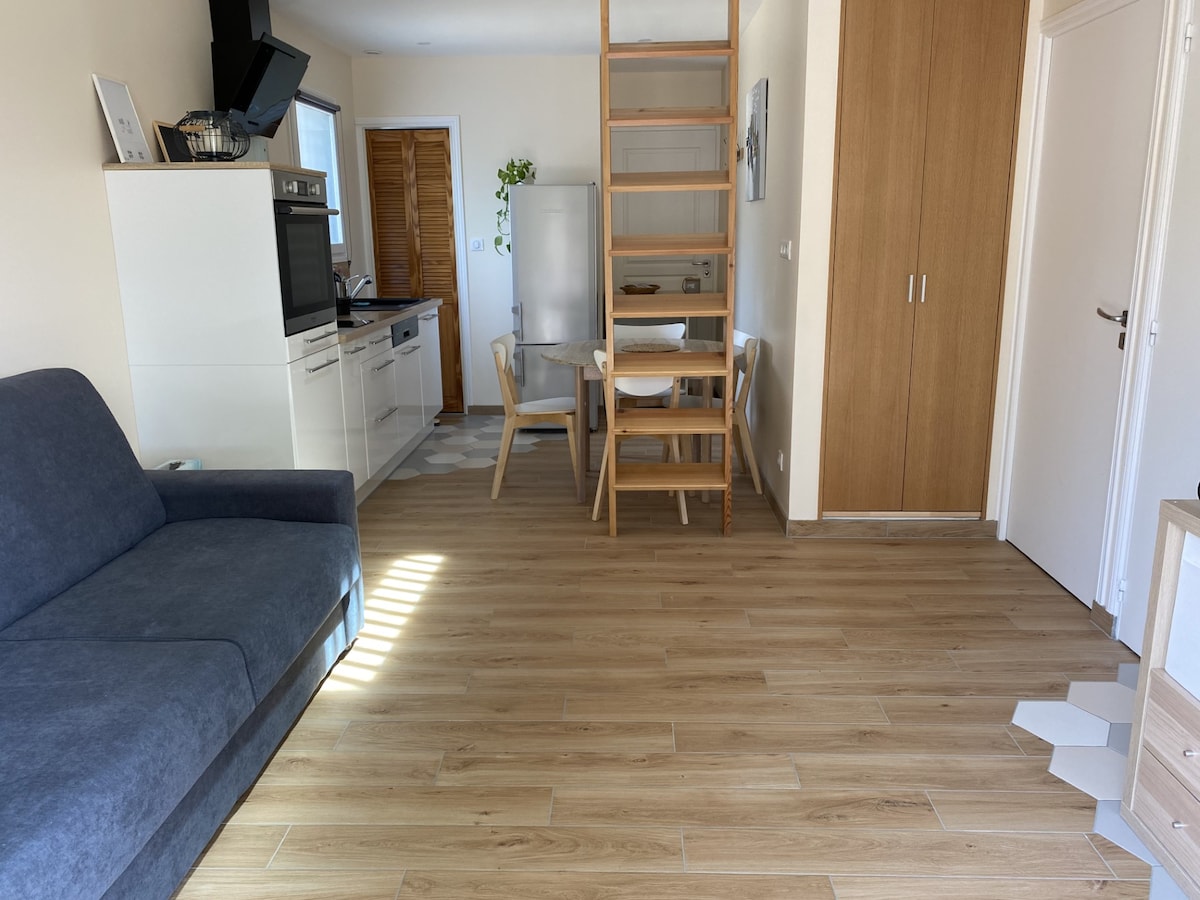 A spacious living area is presented, featuring a comfortable sofa and a dining table. The kitchen is equipped with modern appliances, including a refrigerator and an oven. Natural light illuminates the wood-style flooring, enhancing the airy ambiance.