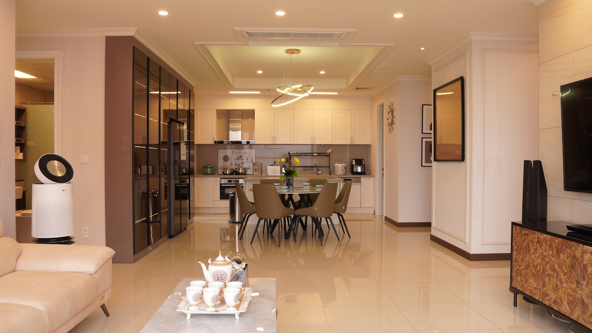 A spacious living area features a modern kitchen equipped with stainless steel appliances and a dining table accompanied by stylish chairs. Ample natural light illuminates the polished tile floor, complemented by elegant decor and contemporary furnishings.