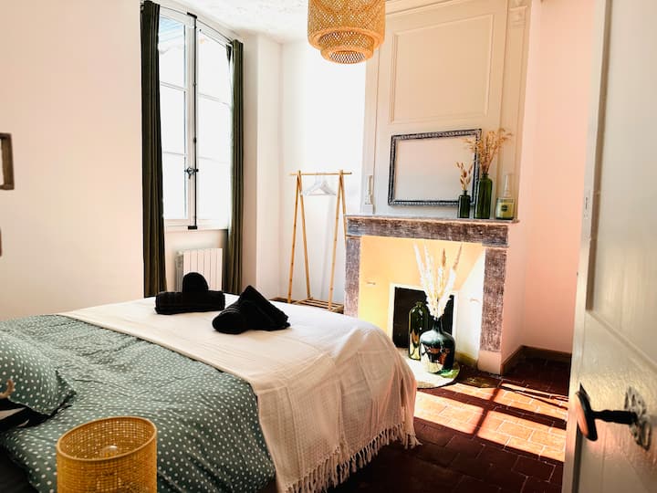 Cette chambre située au 1er étage, est un havre de paix. Elle présente de grandes fenêtres, un lit très confort , et une cheminée ornée. La décoration élégante, avec des touches de vert et de bois, crée une ambiance chaleureuse et accueillante.