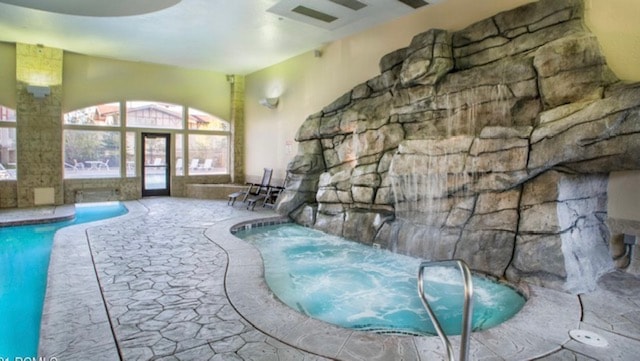 An indoor pool area features a rock-themed water feature cascading down a stone wall. To the side, a hot tub is positioned for relaxation. Large windows allow for natural light and provide views of the outdoor swimming area. Stone flooring adds texture to the space.