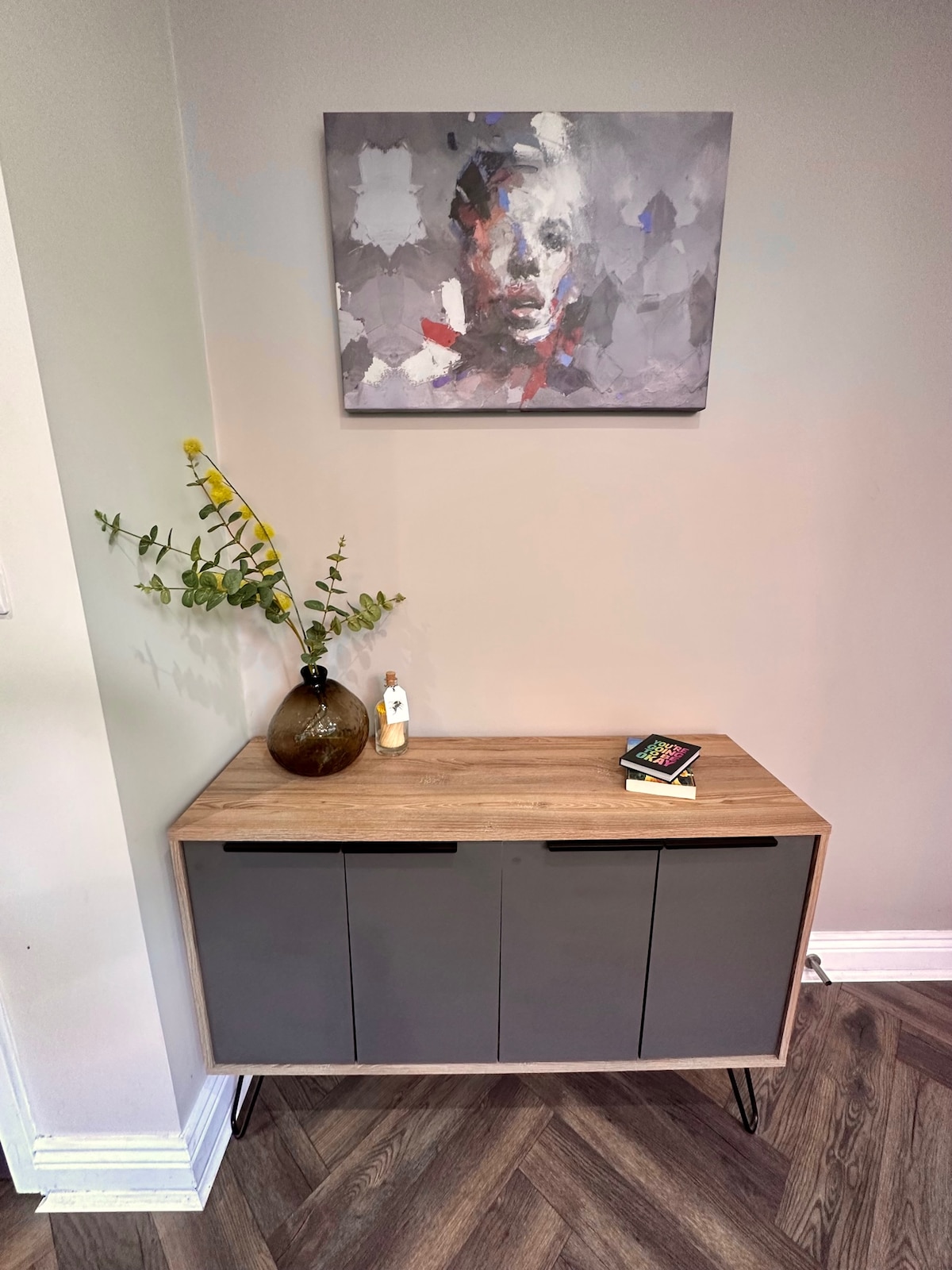 - დახვეწილი კონსოლის კონფიგურაცია თანამედროვე ხელოვნების ნიმუშითა და მინიმალისტური დეკორით, რომ გლუვი შესასვლელი იგრძნოთ
- ხისა და მქრქალი ნაცრისფერი მოპირკეთება საცხოვრებელს სითბოსა და დახვეწილობას მატებს
- სიმწვანისა და კურირებული წიგნების შეხება სტუმართმოყვარე და გააზრებულ კუთხეს ხდის