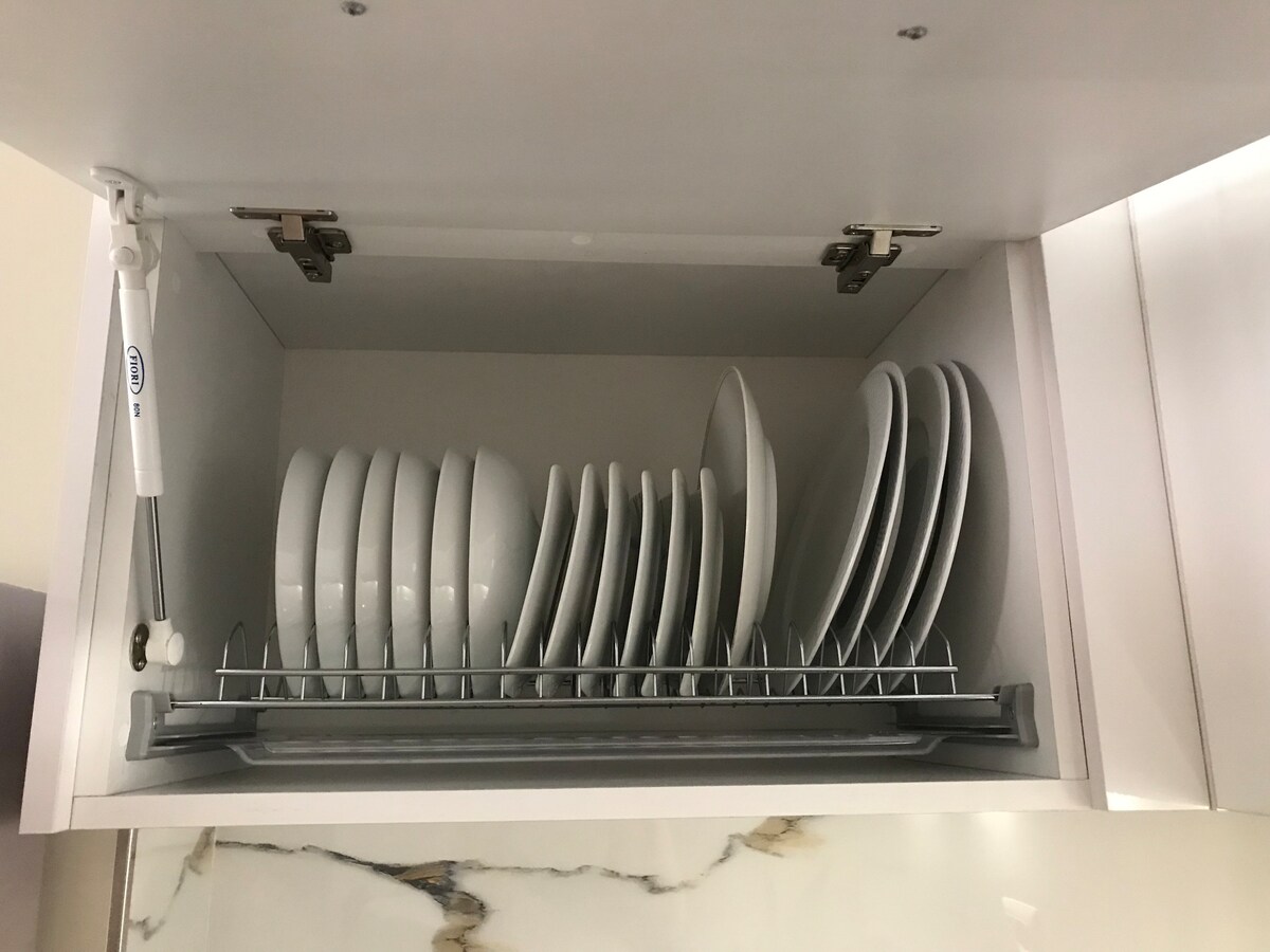 A cabinet is shown with neatly arranged white plates on a rack. The plates are stacked in an organized manner, with a sliding mechanism visible for easy access. The interior is clean and well-maintained, contributing to a functional kitchen space.
