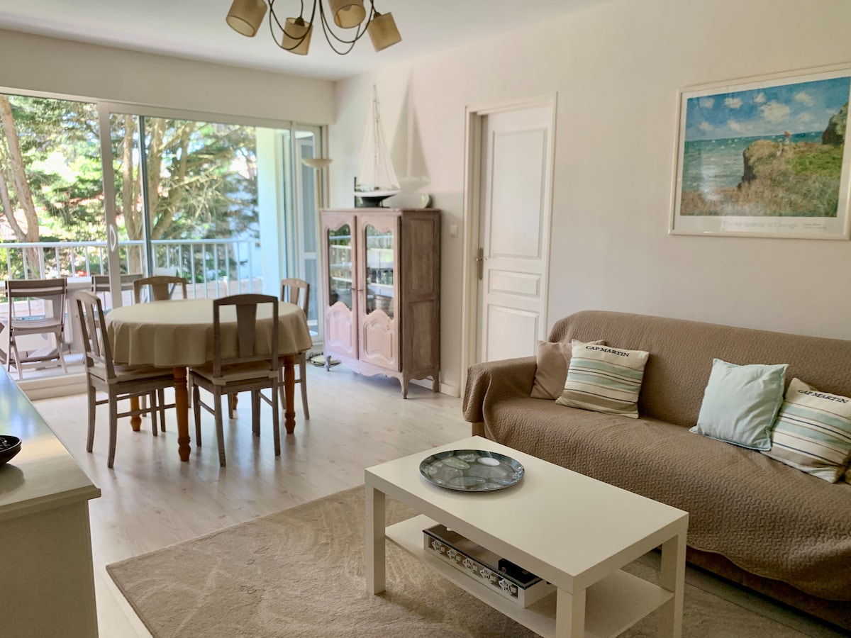 The living area features a comfortable sofa facing a light-colored coffee table. A dining table with chairs is positioned near large sliding glass doors that open to a balcony. Natural light fills the space, complemented by a neutral color palette and tasteful decor.