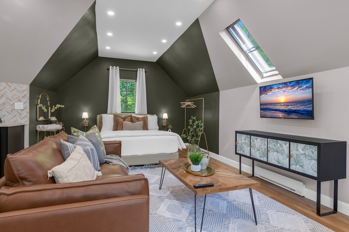 A spacious living area features a comfortable sofa and a wooden coffee table, complemented by a flat-screen TV mounted on the wall. Natural light filters through the skylight and window, illuminating the modern decor that includes a stylish bed and tasteful accents.