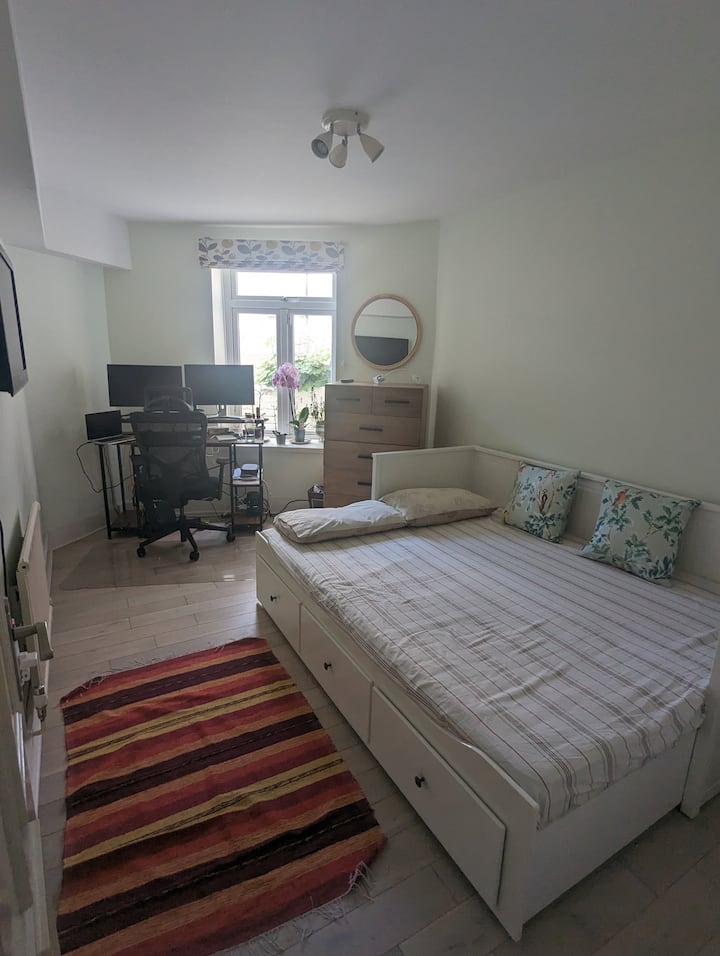 El dormitorio de invitados, con ventanas orientadas al este y un espacio para trabajar privado, tiene una cómoda cama queen, un televisor montado en la pared y un tocador con espejo.
