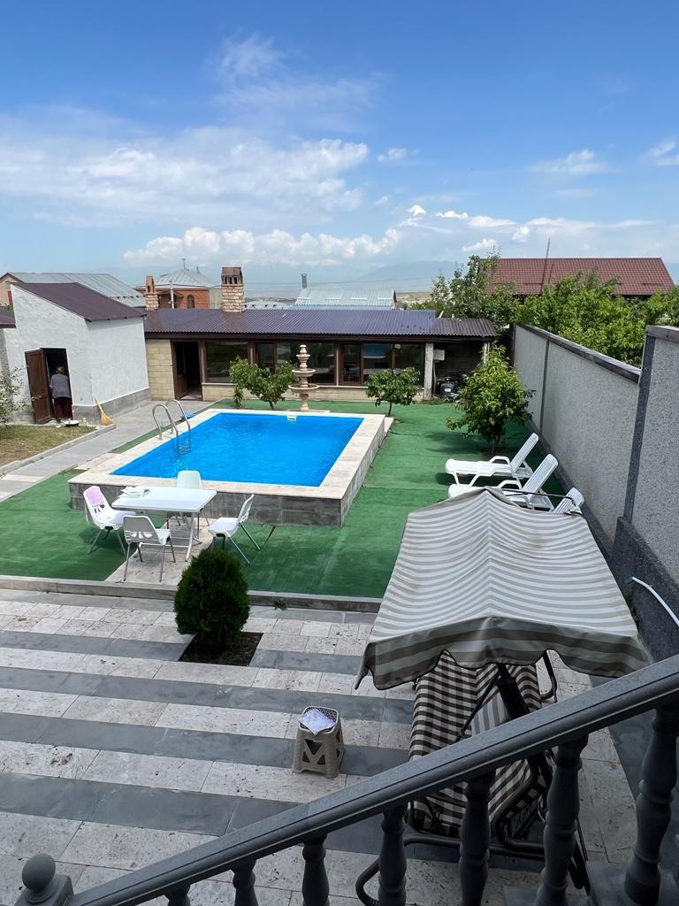 A private outdoor space features a serene swimming pool surrounded by green grass. Sun loungers and a shaded seating area provide options for relaxation. A decorative fountain adds visual interest, and lush greenery offers a sense of privacy in this tranquil environment.