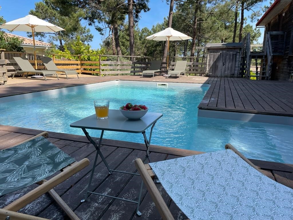 A serene outdoor area showcases a private pool surrounded by wooden decking. Lounge chairs are positioned under umbrellas, inviting relaxation. A small table holds a bowl of strawberries and a glass of juice, adding a touch of leisure to this tranquil setting.