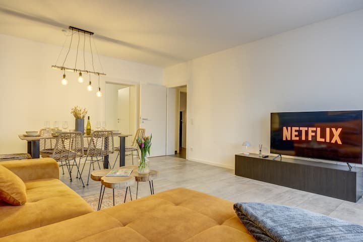 De woonkamer maakt indruk met gezellige en moderne meubels. Naast de eettafel met 6 stoelen is er een grote slaapbank, een smart-tv met streamingdiensten en boeken voor een ontspannen avond.