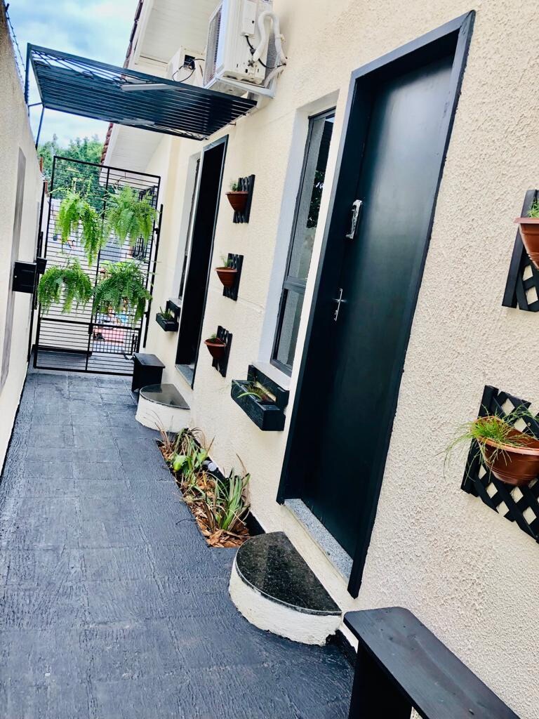 A corridor is lined with dark doors and decorative plant holders. Potted plants are displayed on the walls, adding character. The flooring is dark and smooth, complementing the light-colored walls. A small step is visible near the entrance, enhancing the space's design.