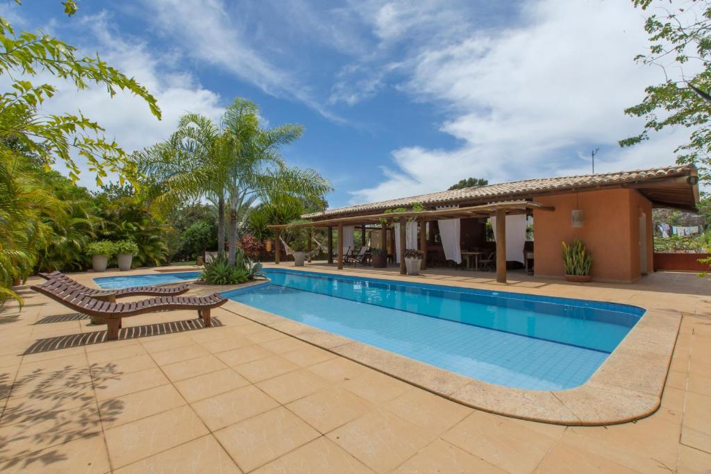 A serene outdoor space featuring a clear swimming pool surrounded by sun loungers and vibrant greenery. A shaded area with a wooden structure provides seating, with plants in decorative pots adding to the natural ambiance. The sky above is partly cloudy, contributing to the tranquil setting.