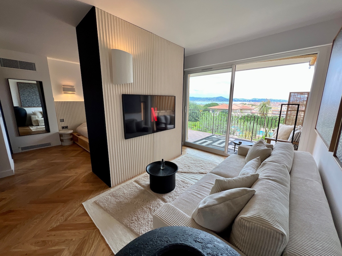 A stylish living area features a modern sofa arranged across from a wall-mounted television, equipped with Netflix access. Large glass doors showcase a scenic view, while a patterned rug and decorative lighting complete the inviting ambiance.