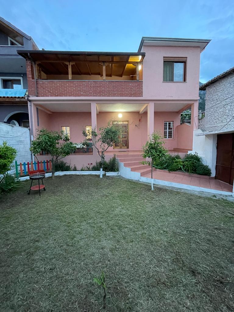 A charming two-story home is set against a twilight sky. The exterior features a pink facade with a covered porch. An inviting garden area with grass and small trees is visible, along with a few steps leading to the main entrance.