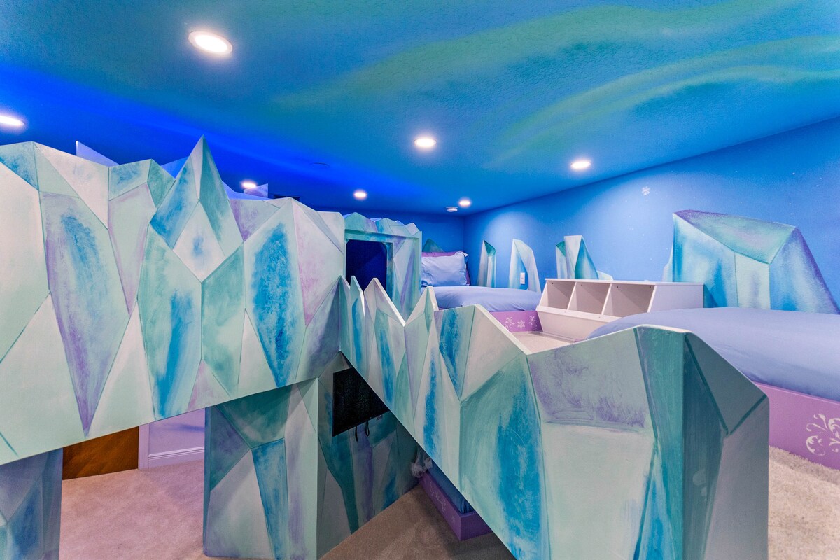 A vibrant, Frozen-themed bedroom is showcased with whimsical ice crystal structures integrated into the design. Cozy sleeping areas are nestled within the creative layout, complemented by a ceiling painted in soothing shades of blue, resembling a winter sky.