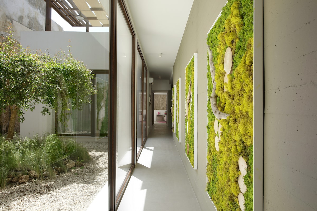 A spacious hallway is lined with large glass doors, allowing natural light to fill the area. Vertical gardens adorned with vibrant green moss and decorative elements are mounted on the walls, creating a refreshing and serene atmosphere.