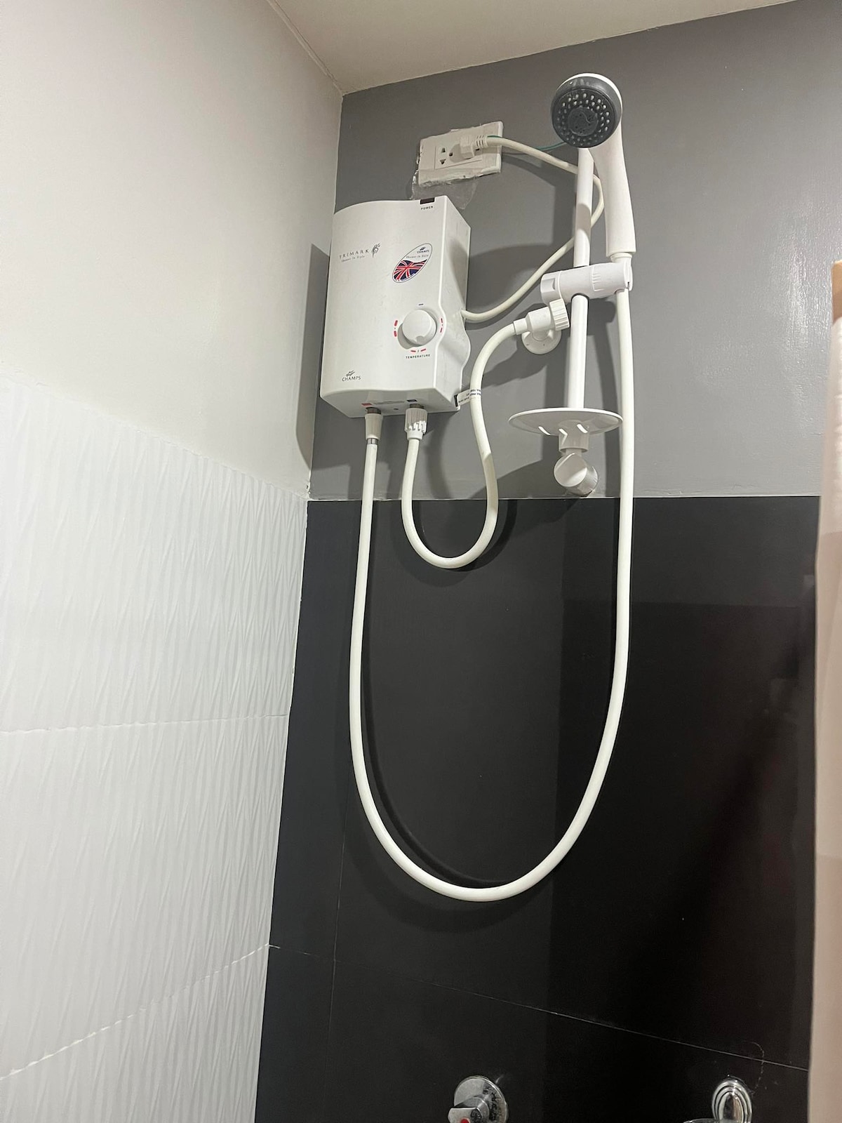 A modern shower fixture is mounted on the wall, featuring a handheld showerhead and a temperature control unit. The walls are finished in a two-tone pattern, displaying white tiles on the left and sleek black tiles on the right.
