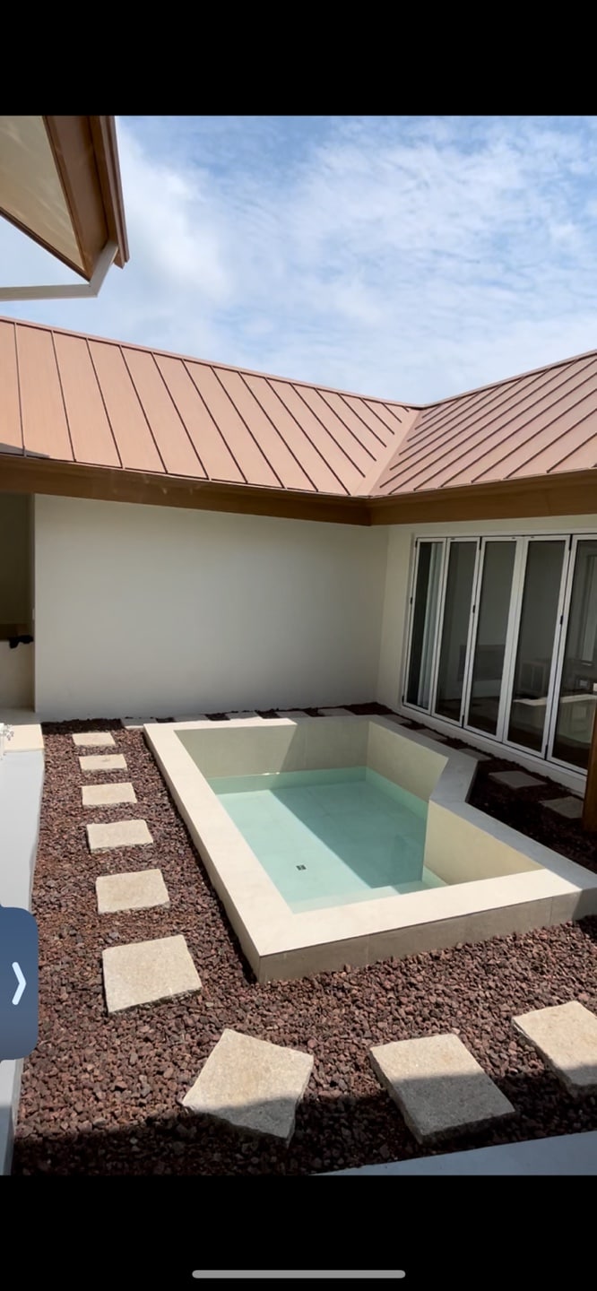 A serene outdoor space is featured, showcasing a shallow pool surrounded by a stone pathway. Natural light reflects off the water, with a backdrop of smooth walls and a slanted roof. Large glass doors are visible, offering a connection to the indoor area.