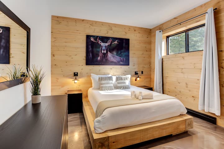 Habitación luminosa con cama tamaño queen, mesitas de noche y decoración inspirada en el bosque.